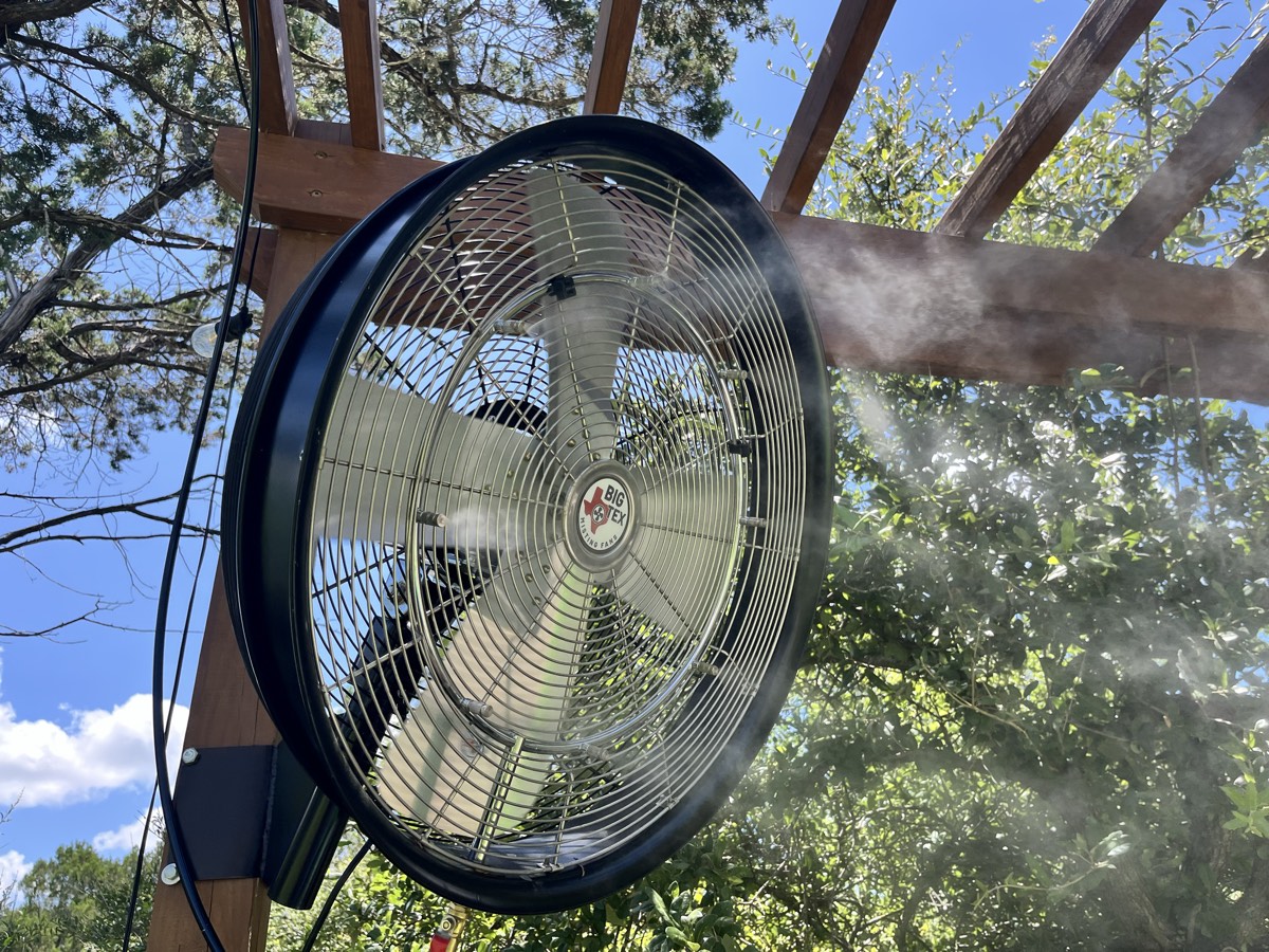 Close-up of a Big Tex high-pressure misting fan throwing a fine mist under the pergola