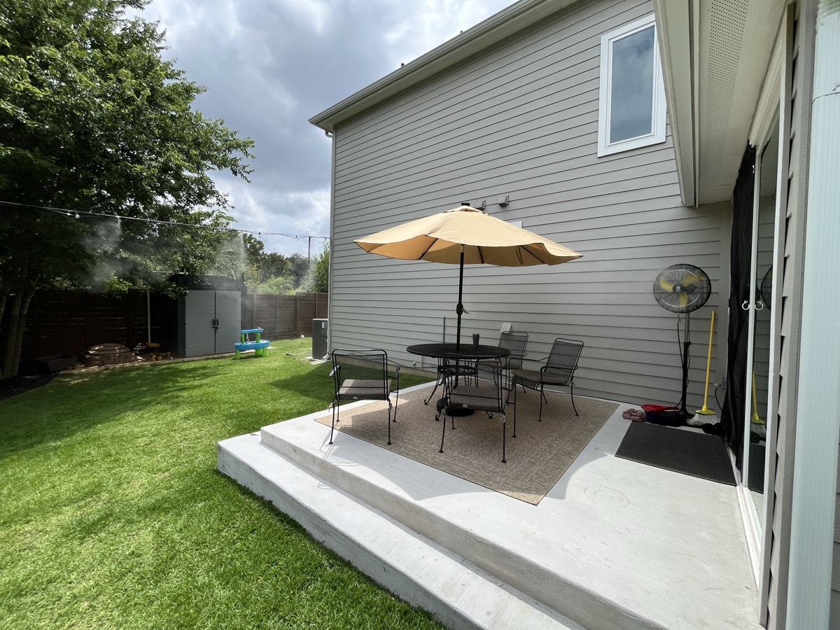 Portable pedestal misting fan cooling a covered patio and outdoor dining set